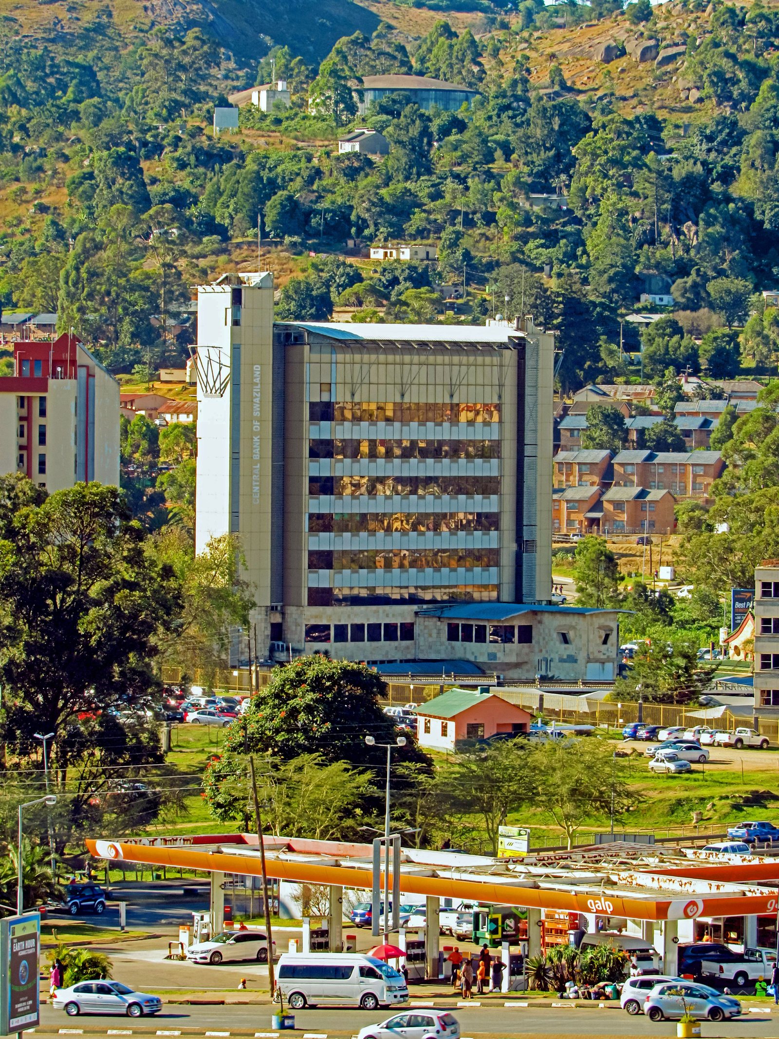 The Central Bank of Eswatini headquarters in Mbabane, ringed by green hills, a fuel station in the foreground.